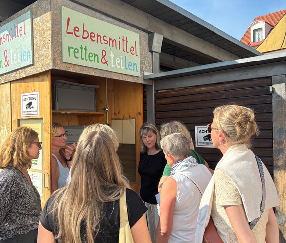 Eine Gruppe Menschen steht vor einem Schrank mit der Aufschrift "Lebensmittel retten und teilen". 