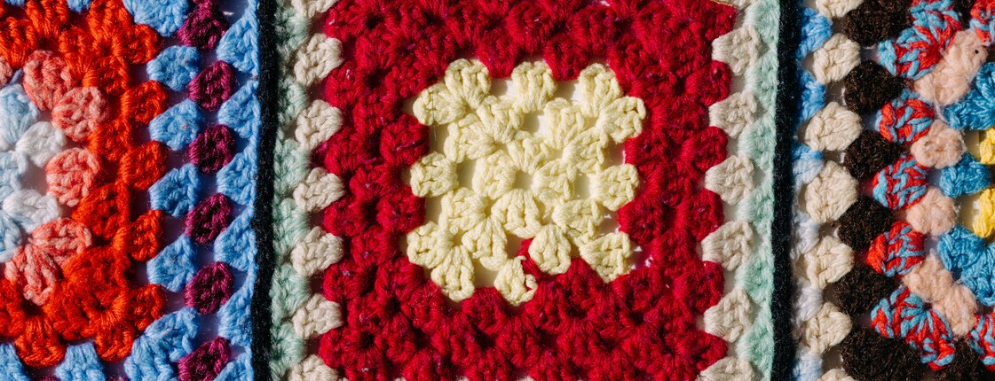 Eine bunte, gehäkelte Topflappendecke.