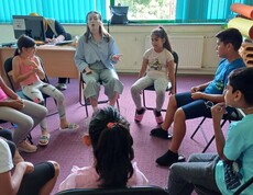 Kinder und eine erwachsene Person sitzen im Sesselkreis und reden