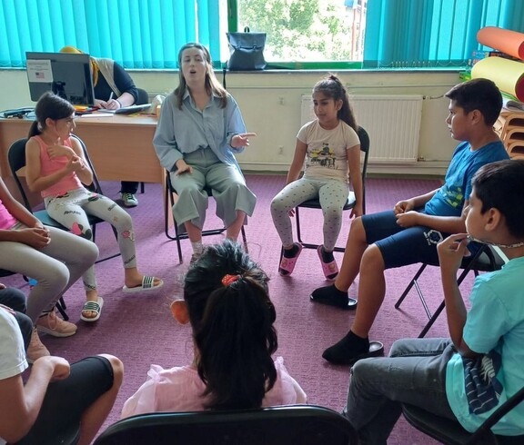 Kinder und eine erwachsene Person sitzen im Sesselkreis und reden