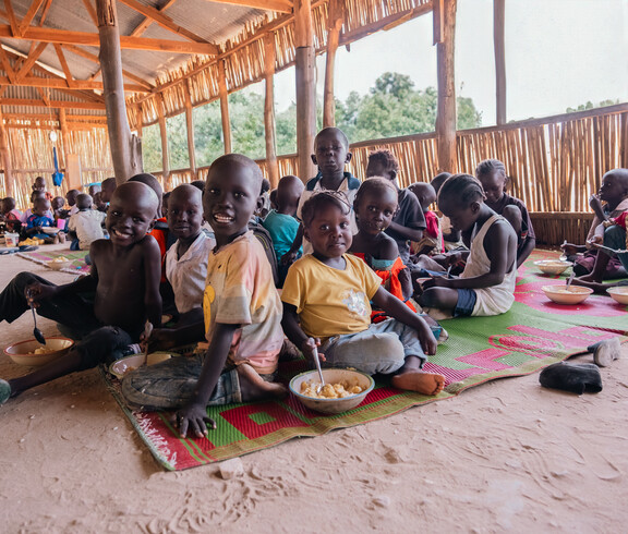 Eine Gruppe südsudanesischer Kinder sitzt am Boden und isst lächelnd
