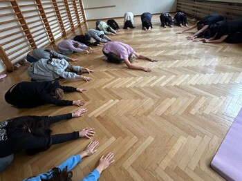 Im Turnsaal machen viele Schüler*innen die Yogaposition des Kindes.
