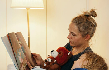 Eine Frau mit Kind die bei einer eingeschalteten Stehlampe ein Buch anschauen