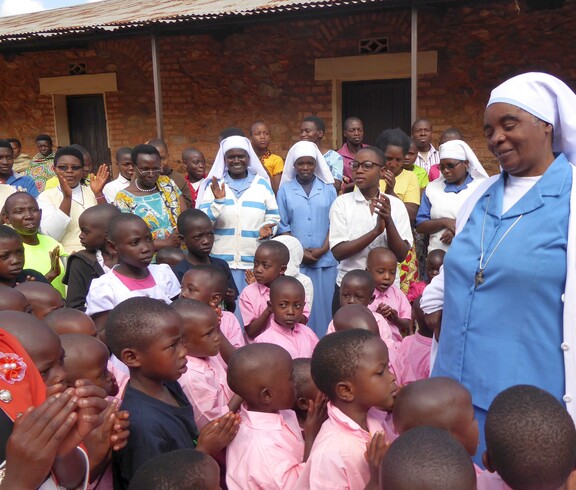Eine Gruppe burundischer Waisenkinder steht da und schaut zu einer burundischen Ordensschwester am Rand. 