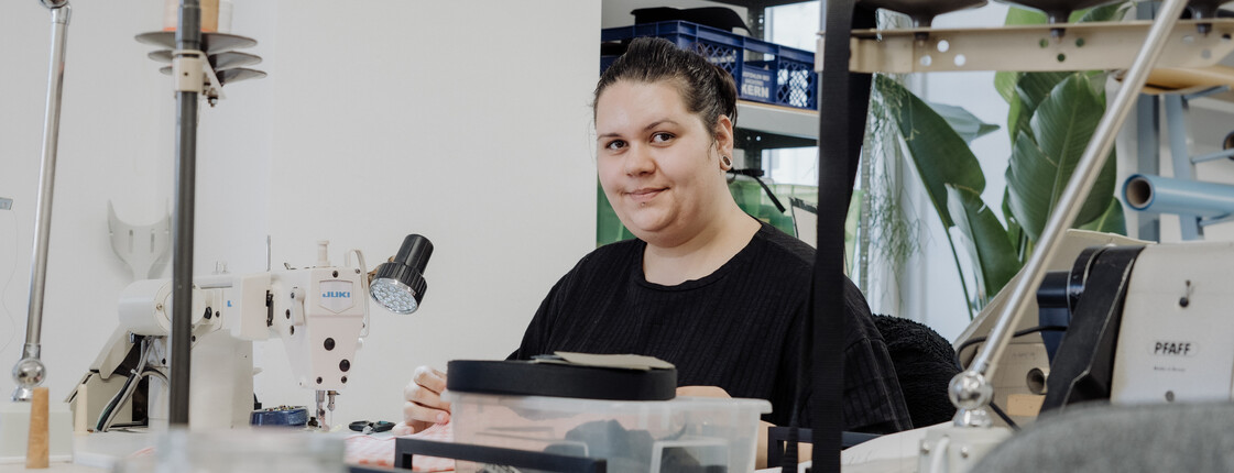 Eine Jugendliche sitzt an einem Arbeitstisch mit Nähmaschine im Caritas Jugendbeschäftigungsprojekt tag.werk
