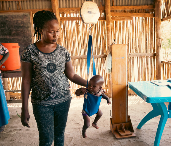 ein südsudanesisches Baby hängt in einer Hängewaage. Daneben steht eine Frau und misst das Ergebnis