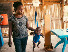 ein südsudanesisches Baby hängt in einer Hängewaage. Daneben steht eine Frau und misst das Ergebnis