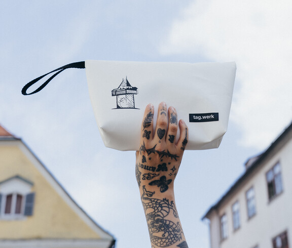 Eine tag.werk-Handtasche der Graz-Kollektion mit Uhrturm als Motiv vor einer Grazer Häuserfassade
