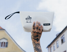 Eine tag.werk-Handtasche der Graz-Kollektion mit Uhrturm als Motiv vor einer Grazer Häuserfassade