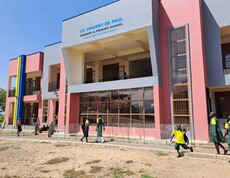 Das neue Schulgebäude von außen, mit freundlichen Farben angemalt und laufenden Schulkindern davor. 