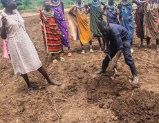 Ein Landwirtschaftlicher Ausbildner zeigt einer Gruppe Frauen, wie sie das Land bearbeiten und ein Beet ausheben. 