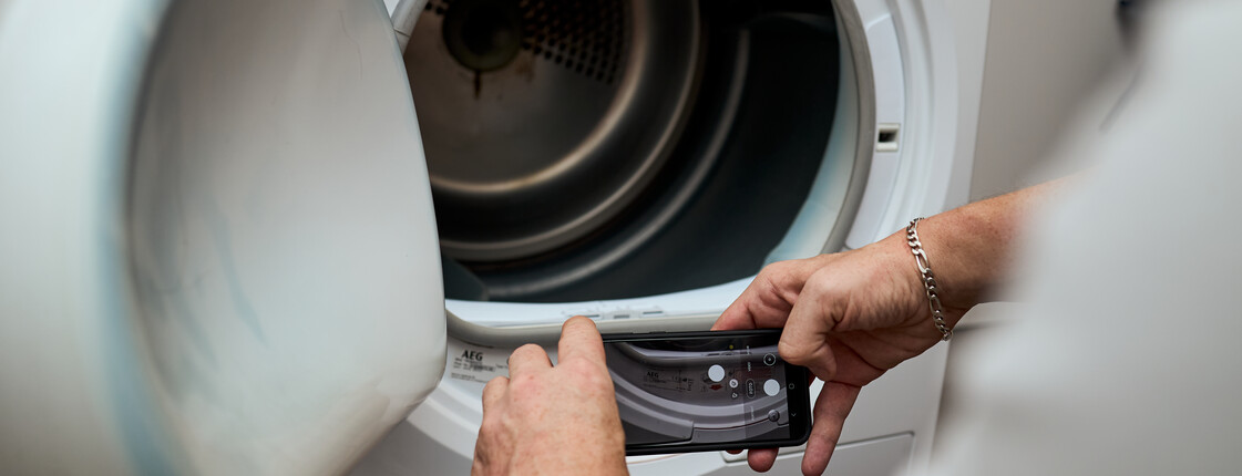 Ein Mitarbeiter der Energiesparberatung macht ein Foto mit deinem Handy von den Gerätedaten einer alten Waschmaschine