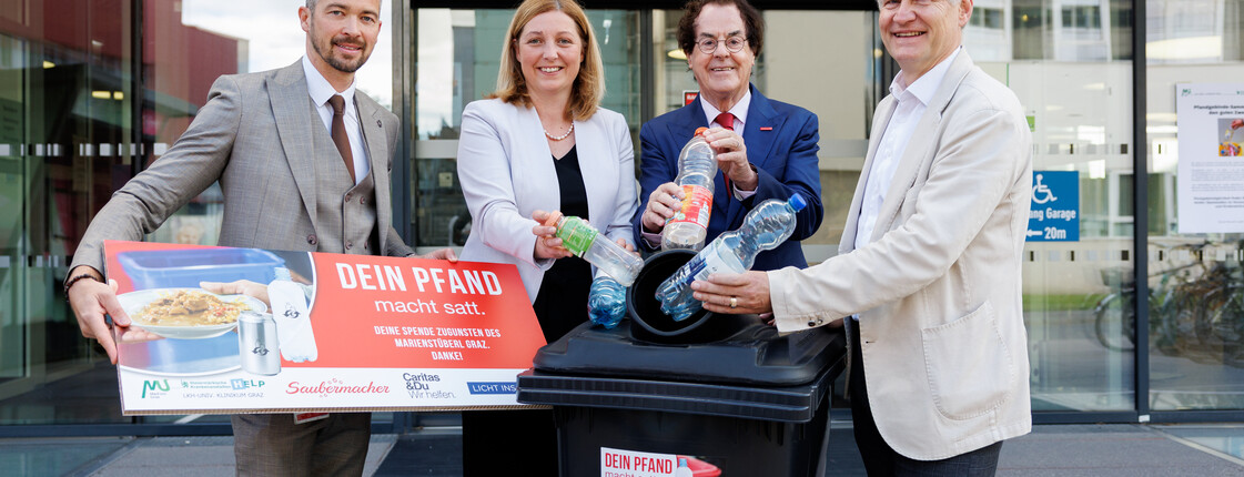 Vier Personen stehen nebeneinander vor einer Mülltonne und werfen symbolisch Plastikflaschen hinein. Von links nach rechts: Michael Kazianschütz (Bereichsleiter Wirtschaft/Logistik, LKH Univ. Klinikum Graz), Nora Tödtling-Musenbichler (Direktorin Caritas Steiermark), Hans Roth (Gründer Saubermacher) und Gebhard Falzberger (Betriebsdirektor LKH Univ. Klinikum Graz). Die Szene steht sinnbildlich für gemeinsames Engagement im Bereich Nachhaltigkeit und Abfallvermeidung.