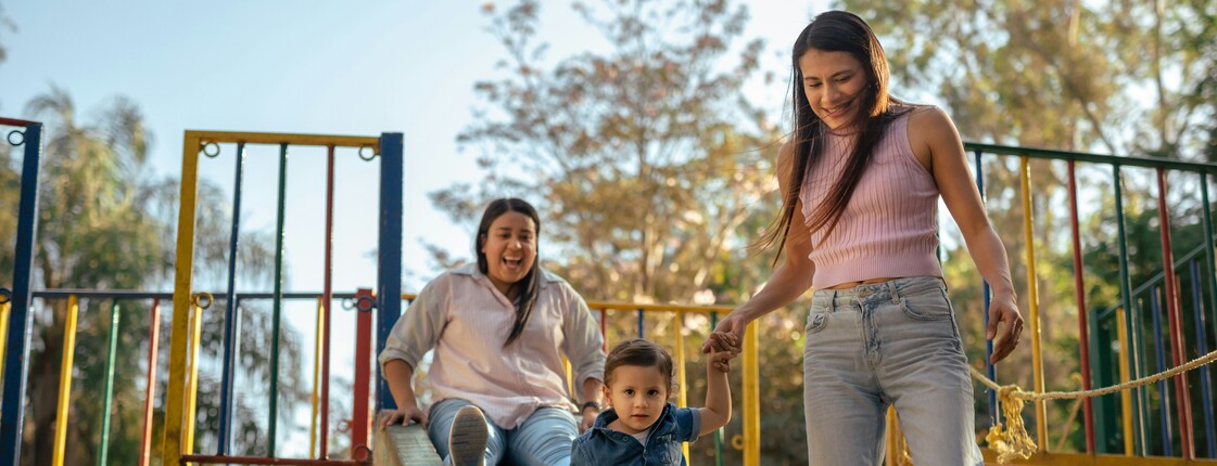 Buddy-Projekt Zwei Frauen spielen mit einem Kind auf einem Spielplatz.