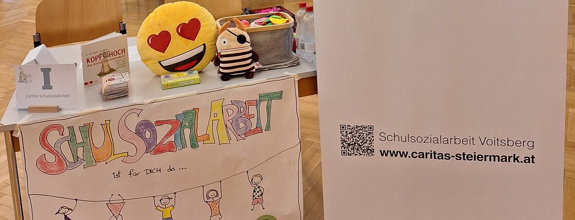 Infotisch der Schulsozialarbeit mit Plüschtieren, Broschüren und einem Banner der Caritas
