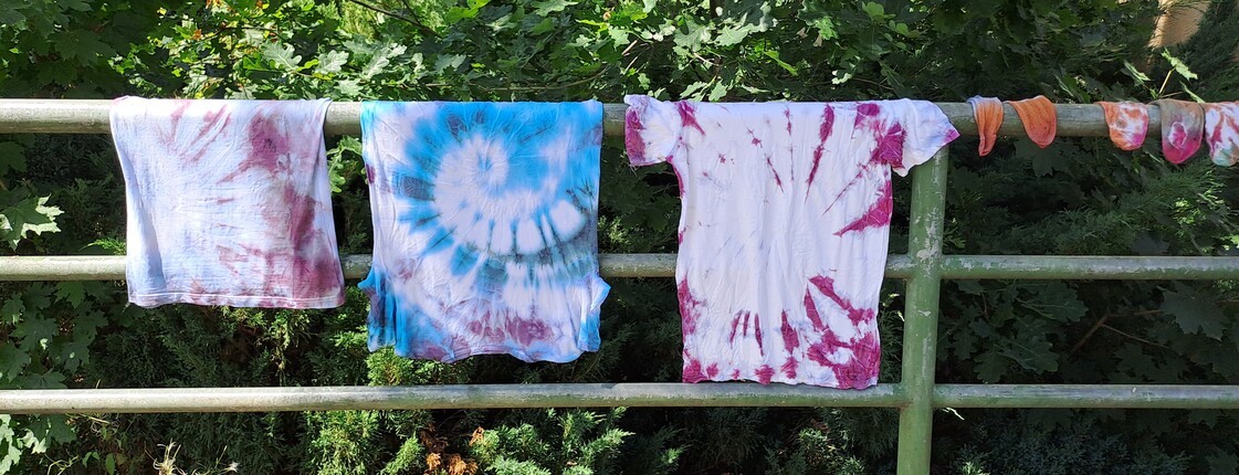 Auf einer Wäscheleine hängen drei bunte T-Shirts in der Schulsozialarbeit gefertigt