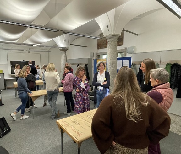 Die Erasmus-Teilnehmenden stehen an verschiedenen Schreibtischen verteilt und diskutieren. 