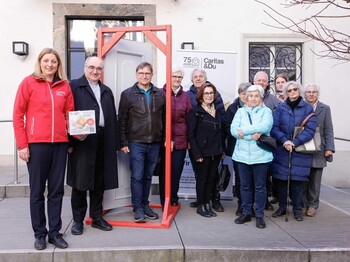 Caritas Steiermark Direktorin Nora Tödtling-Musenbichler steht mit Diözesanbischof Wilhelm Krautwaschl und einer Gruppe von Haussamler:innen im Innenhof der Stadtpfarrkirche Graz um einen geöffneten Türrahmen zusammen.