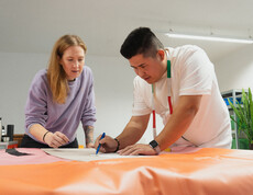 Ein Jugendlicher zeichnet ein Schnittmuster auf einen Plane