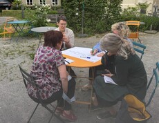 Teilnehmerinnen sitzen um einen Tisch und beschriften ein Plakat. 