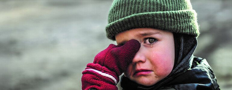Kind mit Mütze und roten Handschuhen wischt sich weinend die Augen ab
