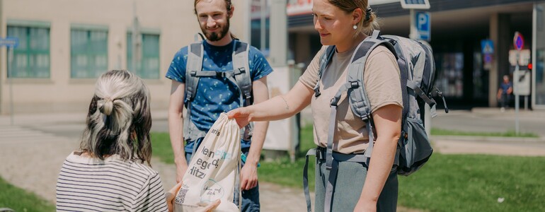 Zwei Streetworker*innen der Caritas Bahnhofsmission übergeben ein Hitzeschutzpaket