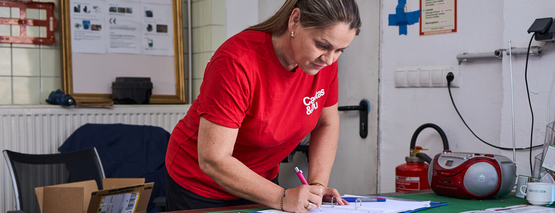 Eine Frau trägt in eine Liste die eingegangenen Sachspenden für Carla ein.