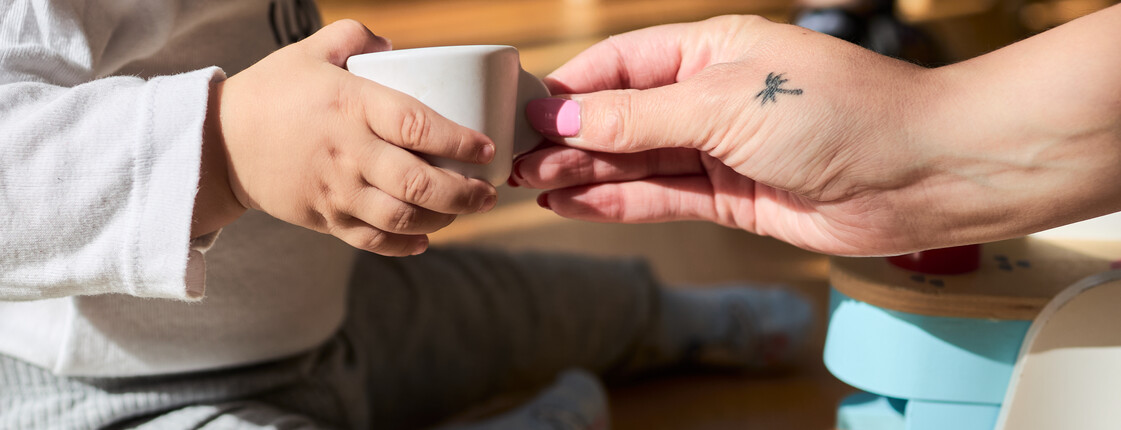 Unsere Angebote im Familienhaus St. Christoph_c_caritas_steiermark Eine erwachsene Hand reicht eine Spieltasse einer Kinderhand.
