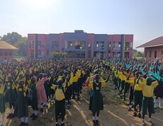Schüler*innen stehen in Schuluniform aufgereiht vor dem Neubau und haben die Arme in der Luft.