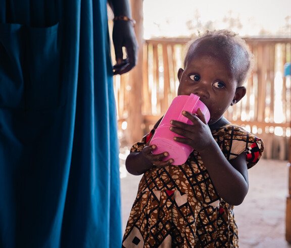 Ein südsudanesisches Kleinkind trinkt aus einem rosa Becher. 