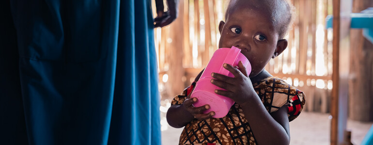 Ein südsudanesisches Kleinkind trinkt aus einem rosa Becher. 