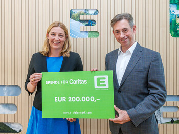 Caritasdirektorin und Energie Steiermark Vorstand halten einen grünen Energie Steiermark Scheck mit der Aufschrift "Spende für Caritas - 200.000€"