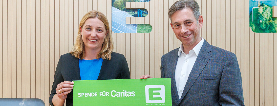 Caritasdirektorin und Energie Steiermark Vorstand halten einen grünen Energie Steiermark Scheck mit der Aufschrift "Spende für Caritas - 200.000€"