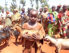 Ein burundisches Kind steht vor einer Gruppe Frauen und trägt eine Ziege im Arm. 