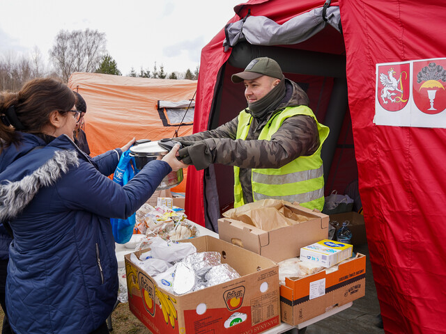 Mitarbeiter der Caritas Polen übergibt einer Frau einen Kochtopf, um ihn herum Lebensmittel