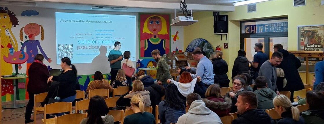 Vortragssituation in einem Klassenzimmer, im Publikum viele Eltern, vor einem Beamerbild der Vortragende