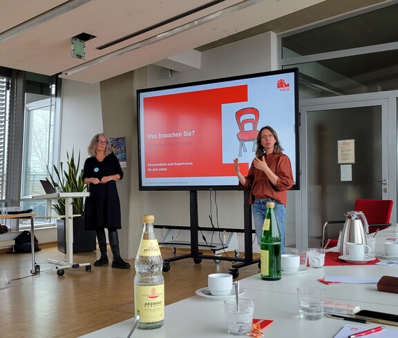 2 Frauen referieren vor einem Bildschirm 