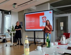 2 Frauen referieren vor einem Bildschirm 