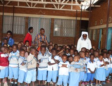 Eine Gruppe burundischer Kindergartenkinder steht mit Blick zur Kamera. Ein paar Ordensschwestern sowie andere Frauen sind im Hintergrund. 
