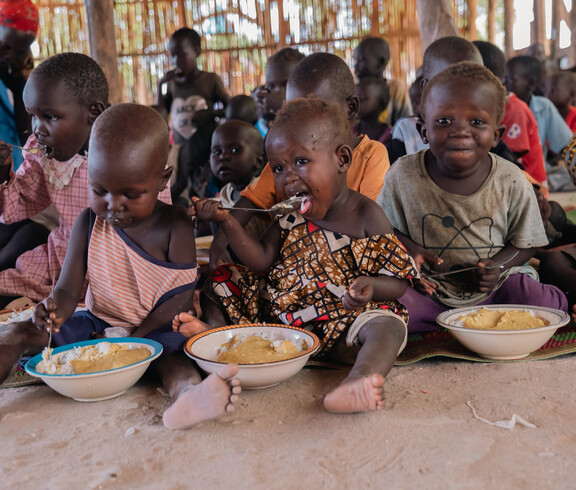 südsudanesische Kinder sitzen am Boden mit gefüllten Tellern vor sich und essen