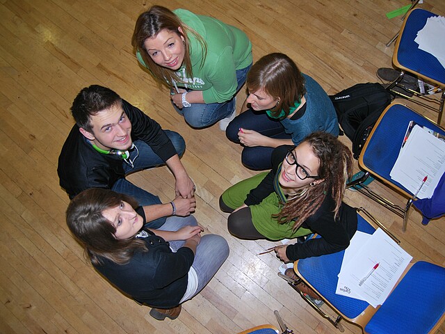 Fünf Jugendliche sitzen in einem Kreis am Boden.