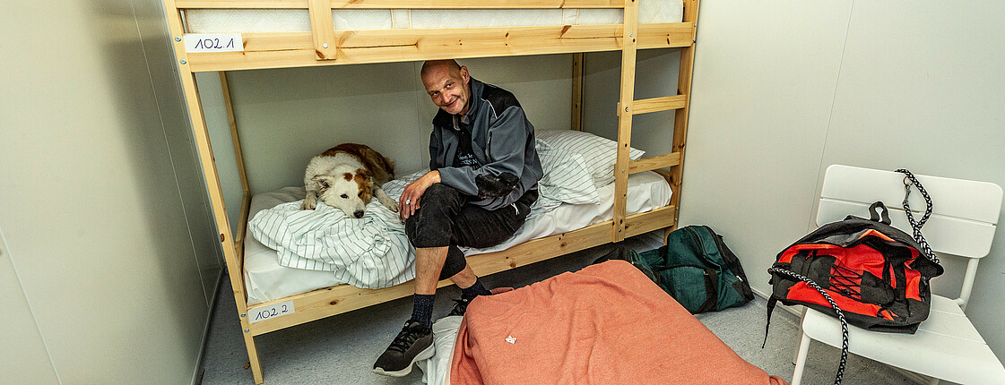 Mann sitzt mit seinem Hund im Bett der Arche 38