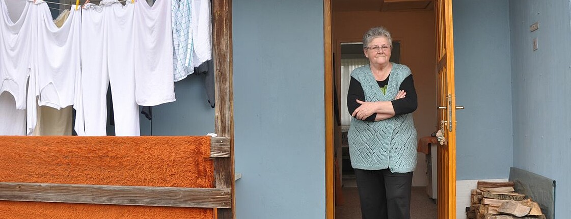 Ein ältere Frau steht am Eingang ihres Hauses.