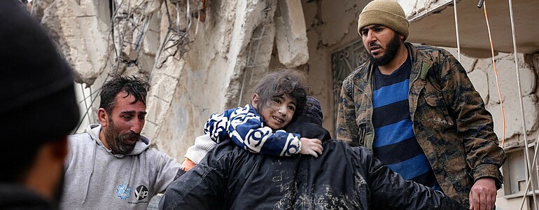 Ein Mädchen auf dem Arm eines Mannes in den Trümmern des Erdbebens, verzweifelte Männer stehen drumherum