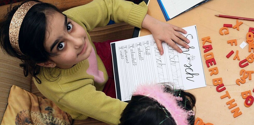 Ein Mädchen lernt mit Buchstaben und blickt zur Kamera hinauf.