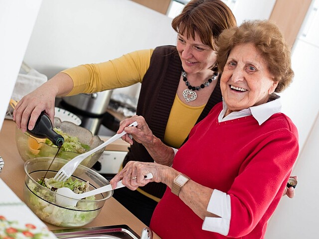 Zwei Frauen machen Salat und lachen.