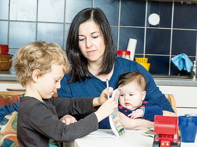 Eine Mutter sitzt mit ihren zwei Kindern an einem Küchentisch.