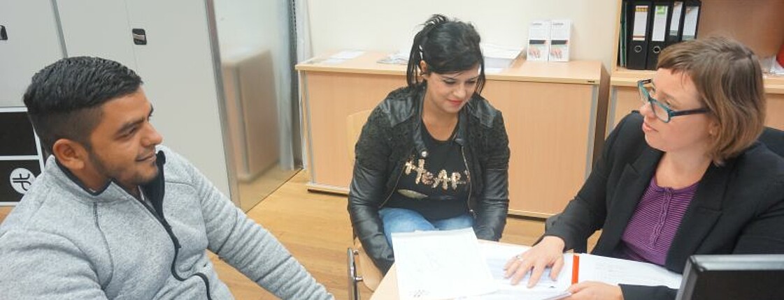 In einer Beratungsstunde des Projektes EMRO werden ein Roma und eine Romnia von einer Projektmitarbeiterin zum Thema Arbeitsmarktintegration beraten.