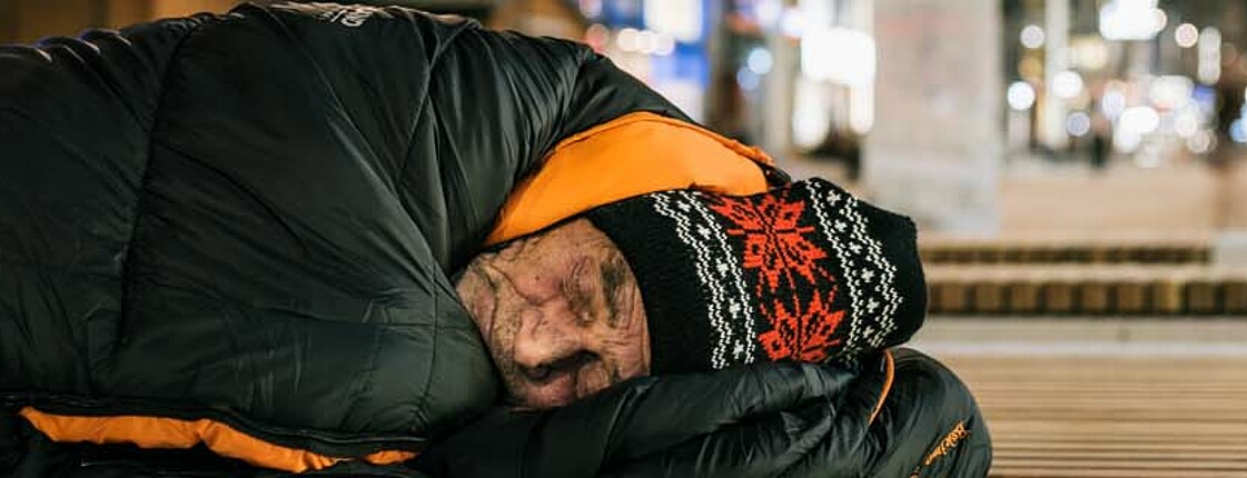 Mann mit Mütze und Schlafsack übernachtet auf Straße 